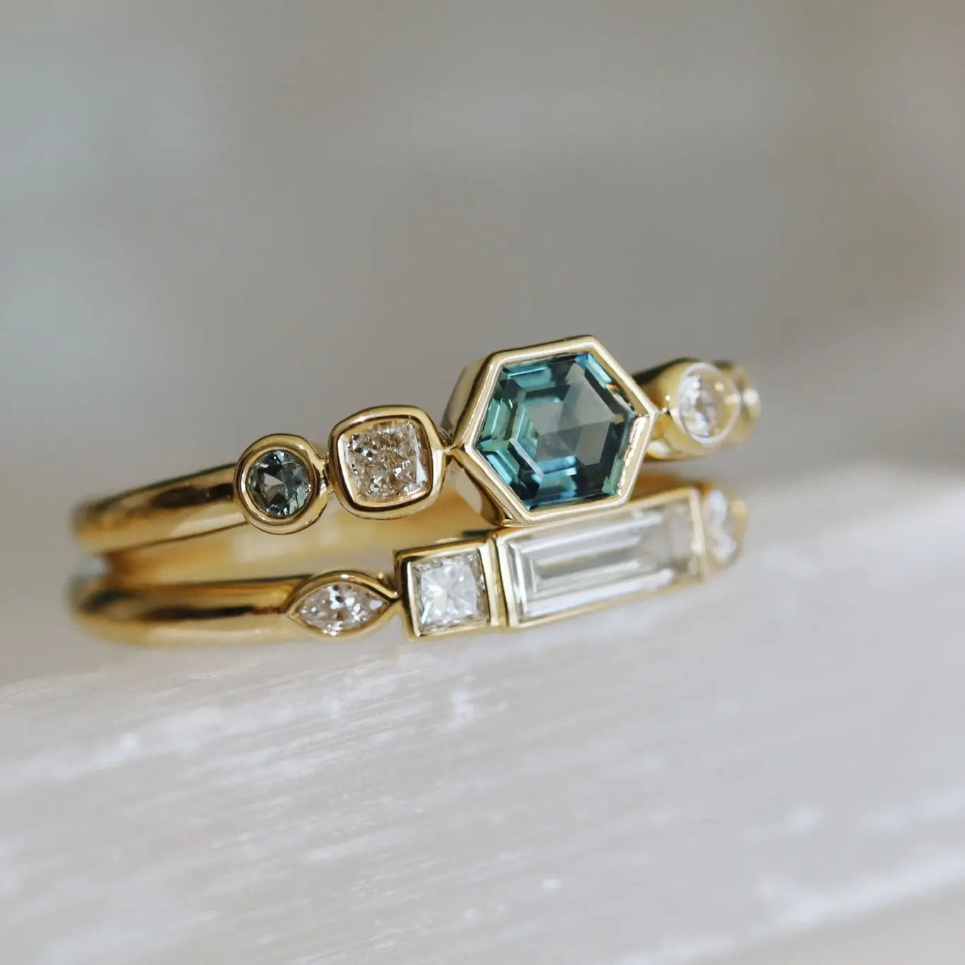 Two gold rings with gemstones on a light background