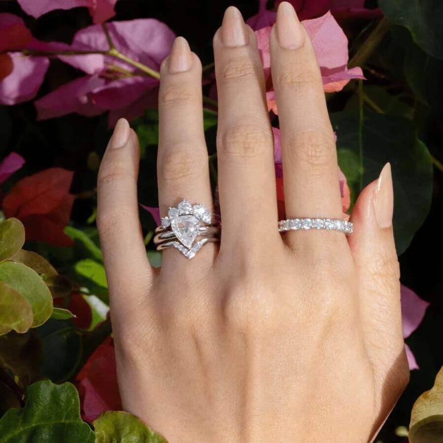 Close up of hand against flowers, featuring a Marrow Fine white diamond engagement ring stack and a pointer finger white diamond ring.