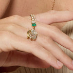 Close-up of a hand wearing two gold rings with gemstones on a neutral background