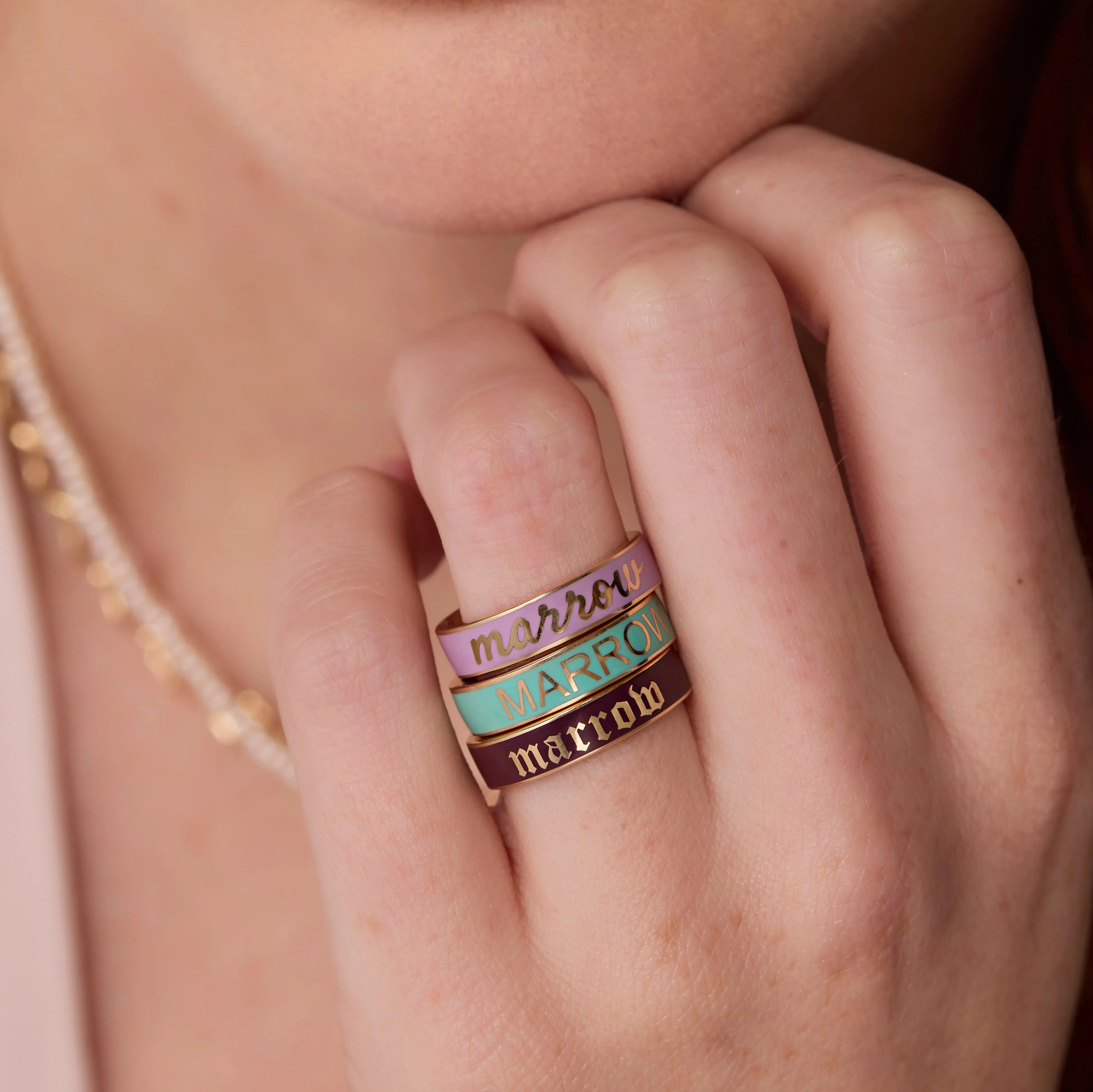 Close up of hand with 3 Marrow custom enamel bands stacked together, all different colors