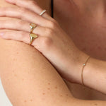 Close-up of a person's arm with gold rings and bracelet on a neutral background