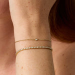 Close-up of a person's wrist wearing two gold bracelets with a blurred background