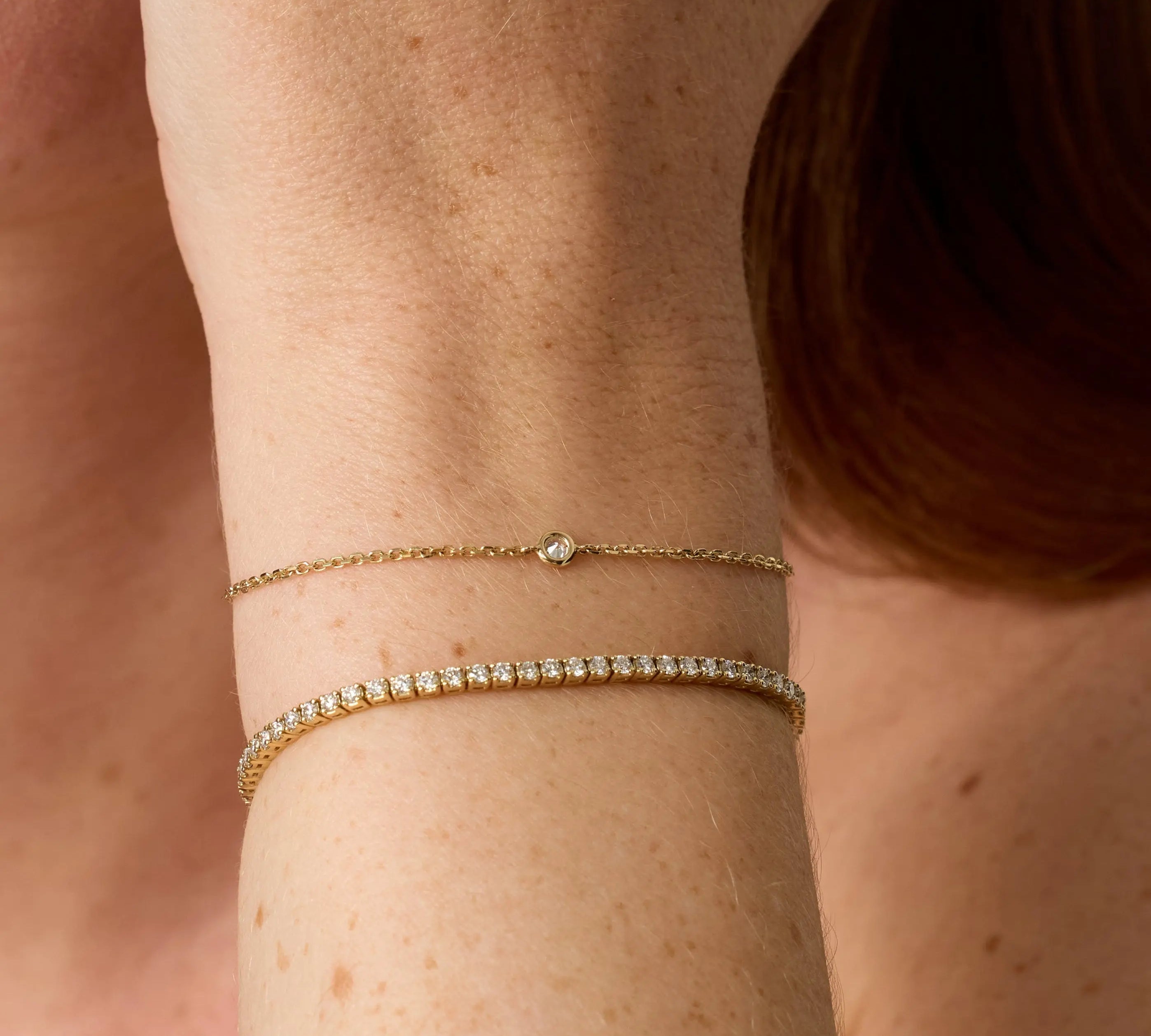 Close-up of a person's wrist wearing two gold bracelets with a blurred background