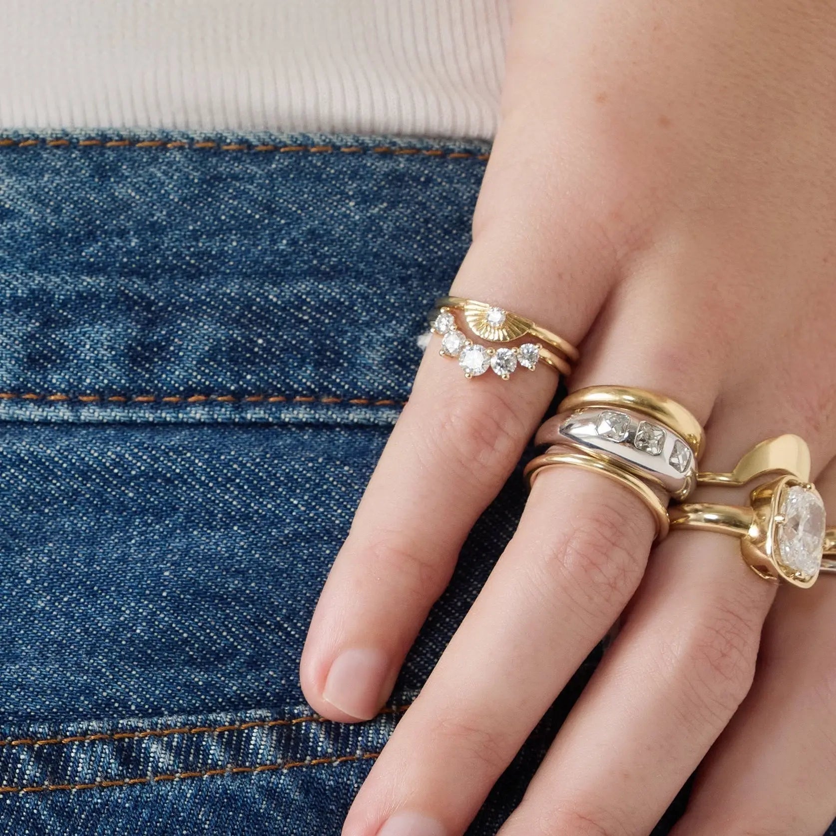 Hand wearing multiple gold rings with gemstones against a denim background