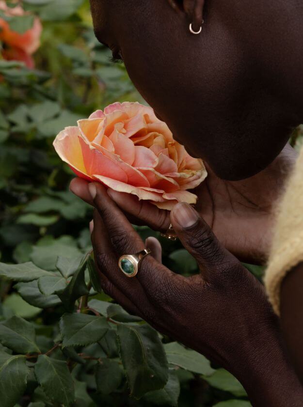 Close up of man smelling a flower wearing Marrow Fine jewelry.