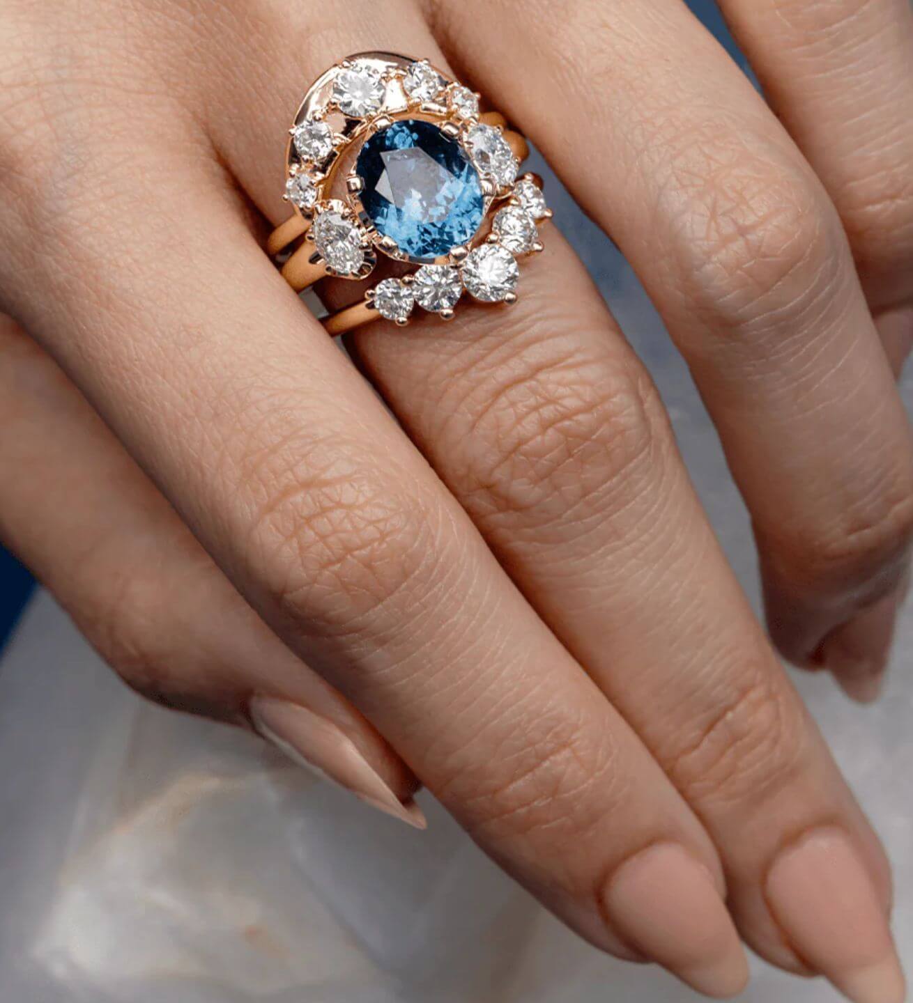 Close up of woman's hand wearing a large Montana Sapphire cocktail ring, in addition to two white diamond bands on either side of the ring.