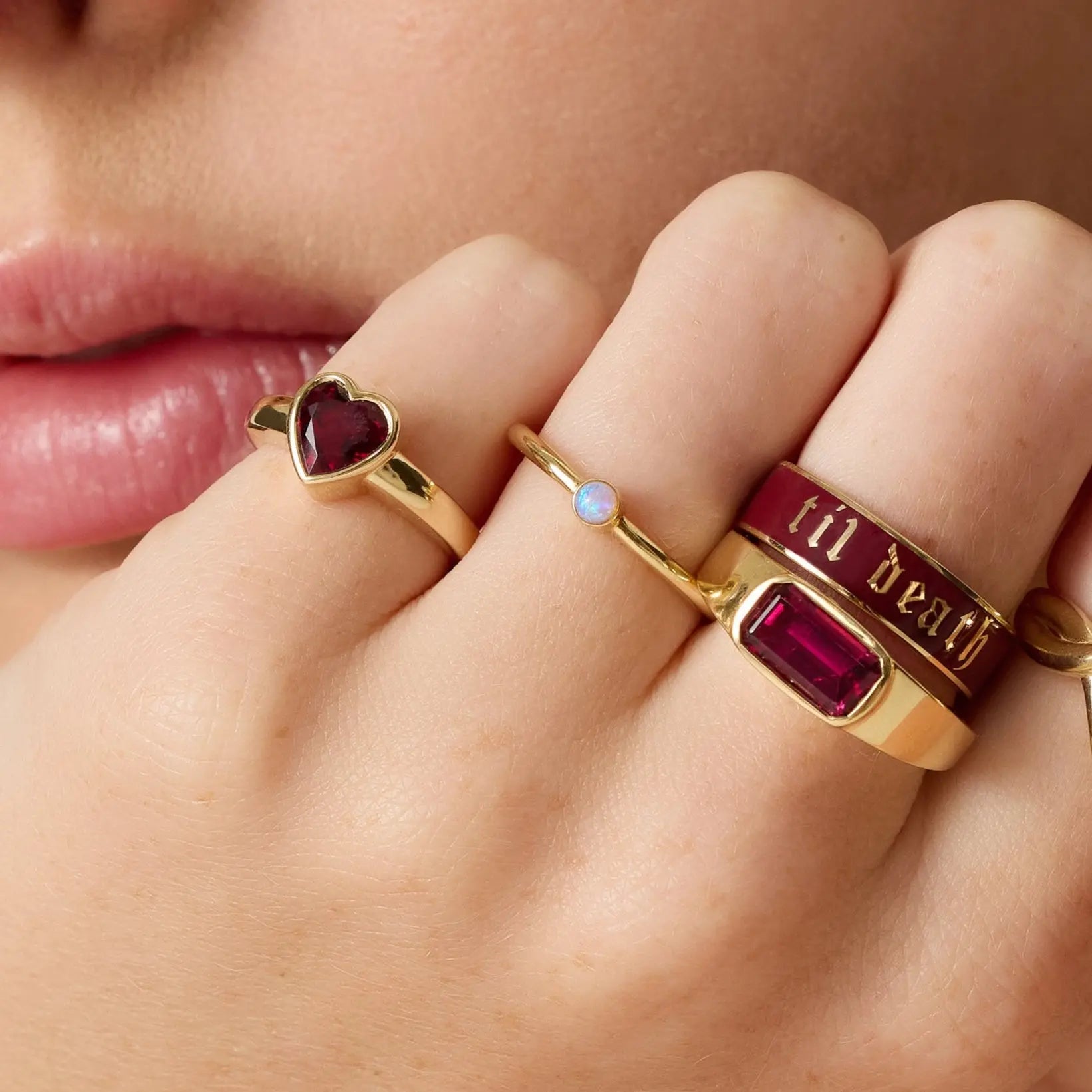 Close-up of a hand wearing multiple gold rings with gemstones and text.
