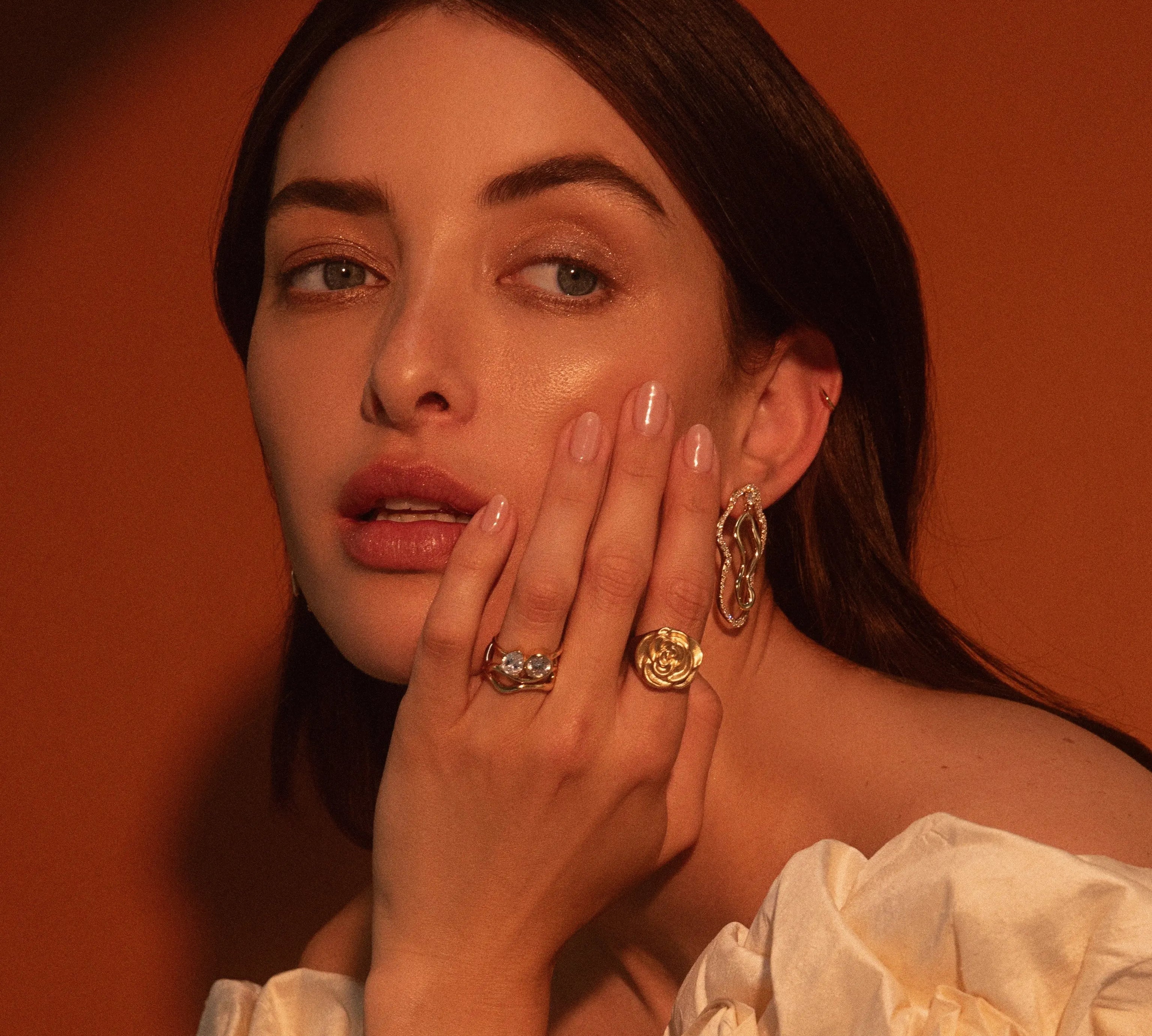 Close up of woman resting hand against her face, highlighting Marrow Fine rings and earrings styled