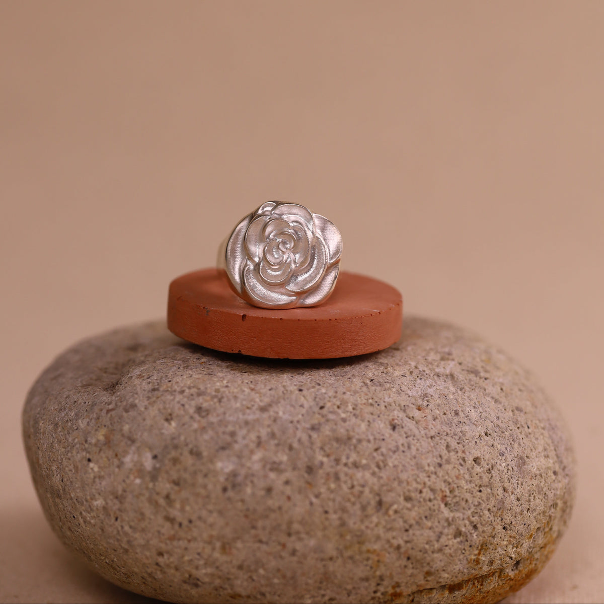 Silver ring with a rose design on a red stone with a beige background