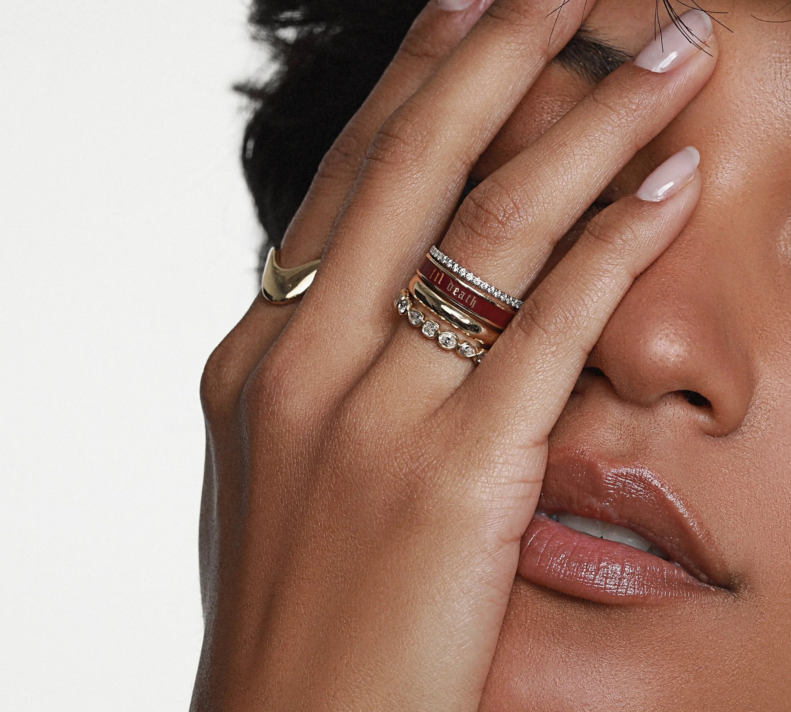 Close up of woman's hand resting on her face, featuring multiple Marrow Fine Rings