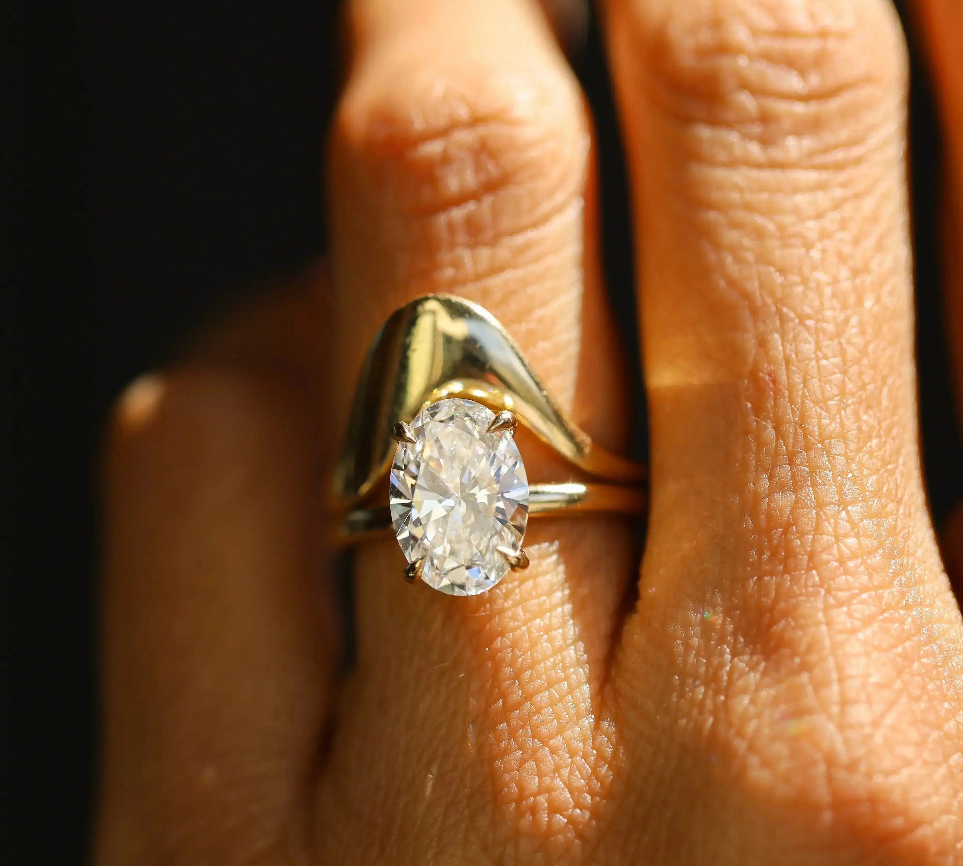 Gold ring with a diamond on a person's finger against a dark background