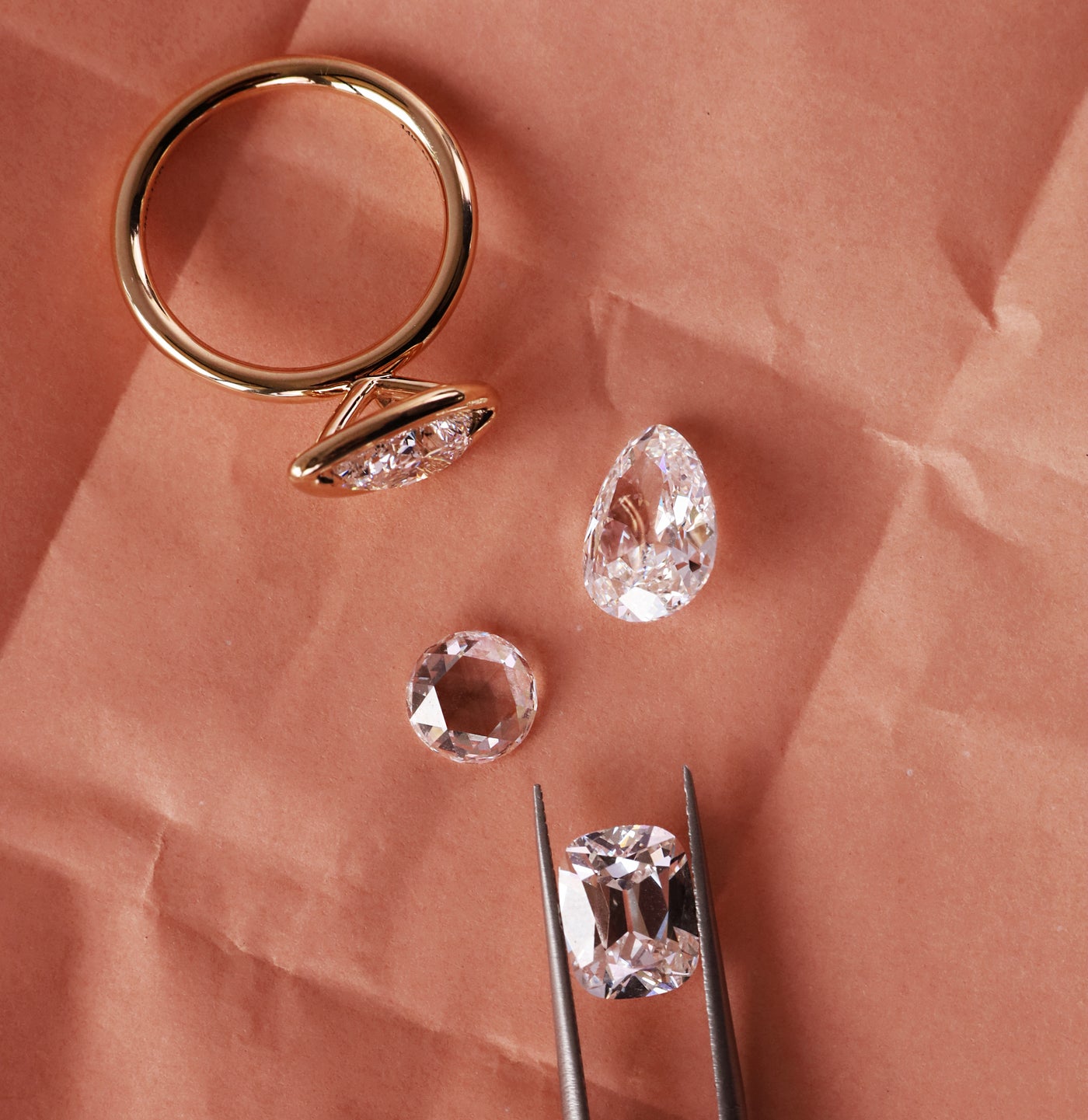 flat lay of gold ring with loose diamonds on a crinkly pink background