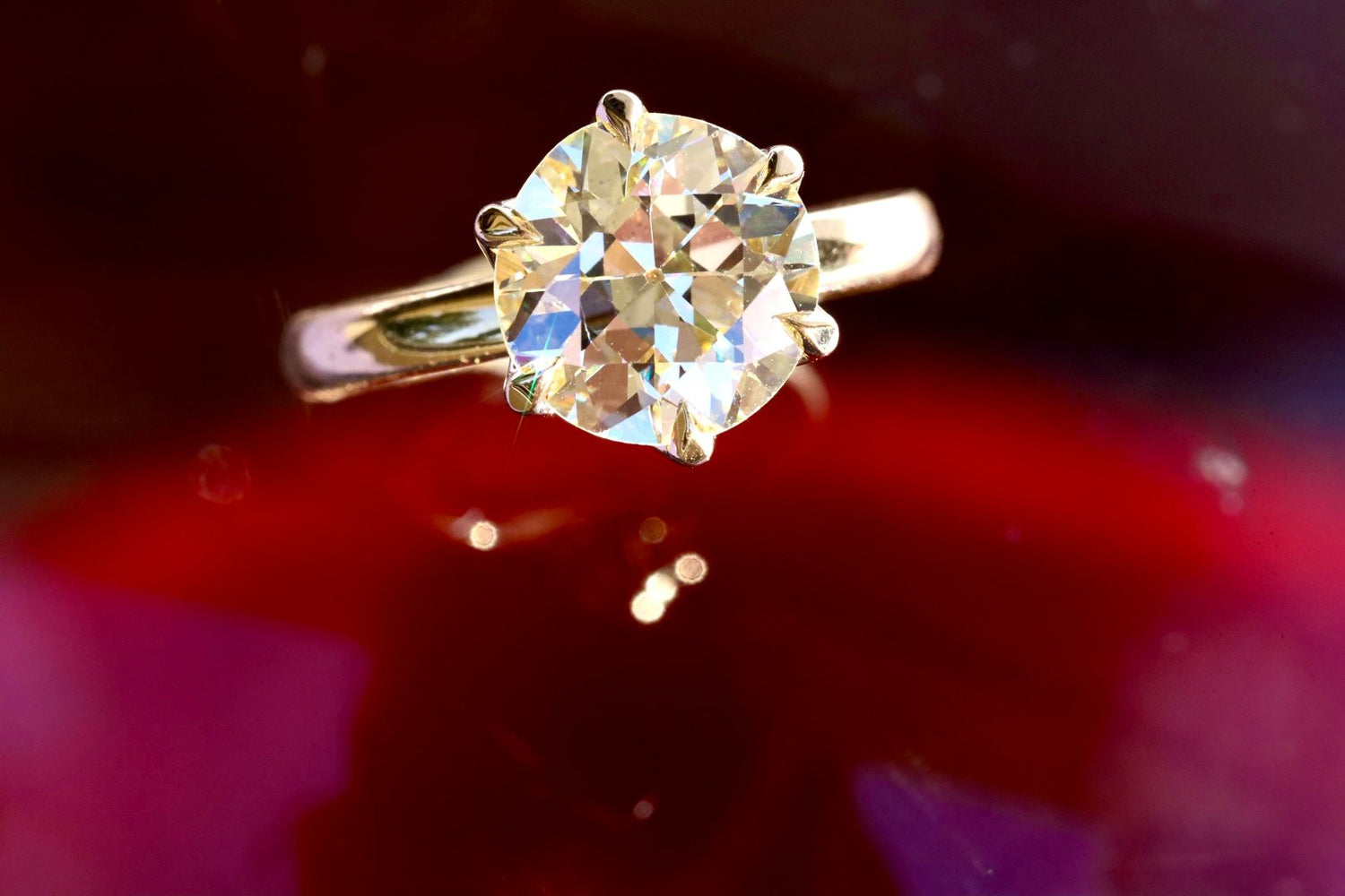 close up of an old European cut diamond engagement ring against a blurry red background