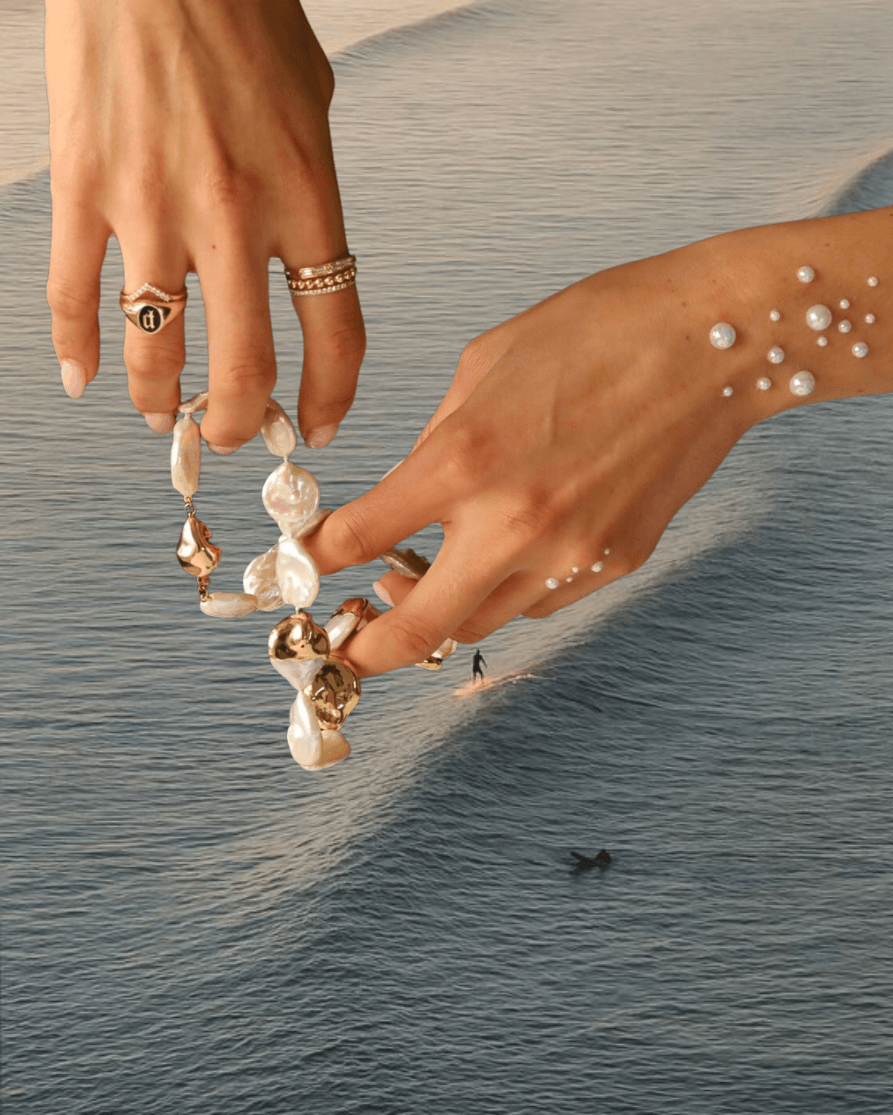 woman's hands holding Marrow pearl necklace with Marrow rings, overlayed on ocean image
