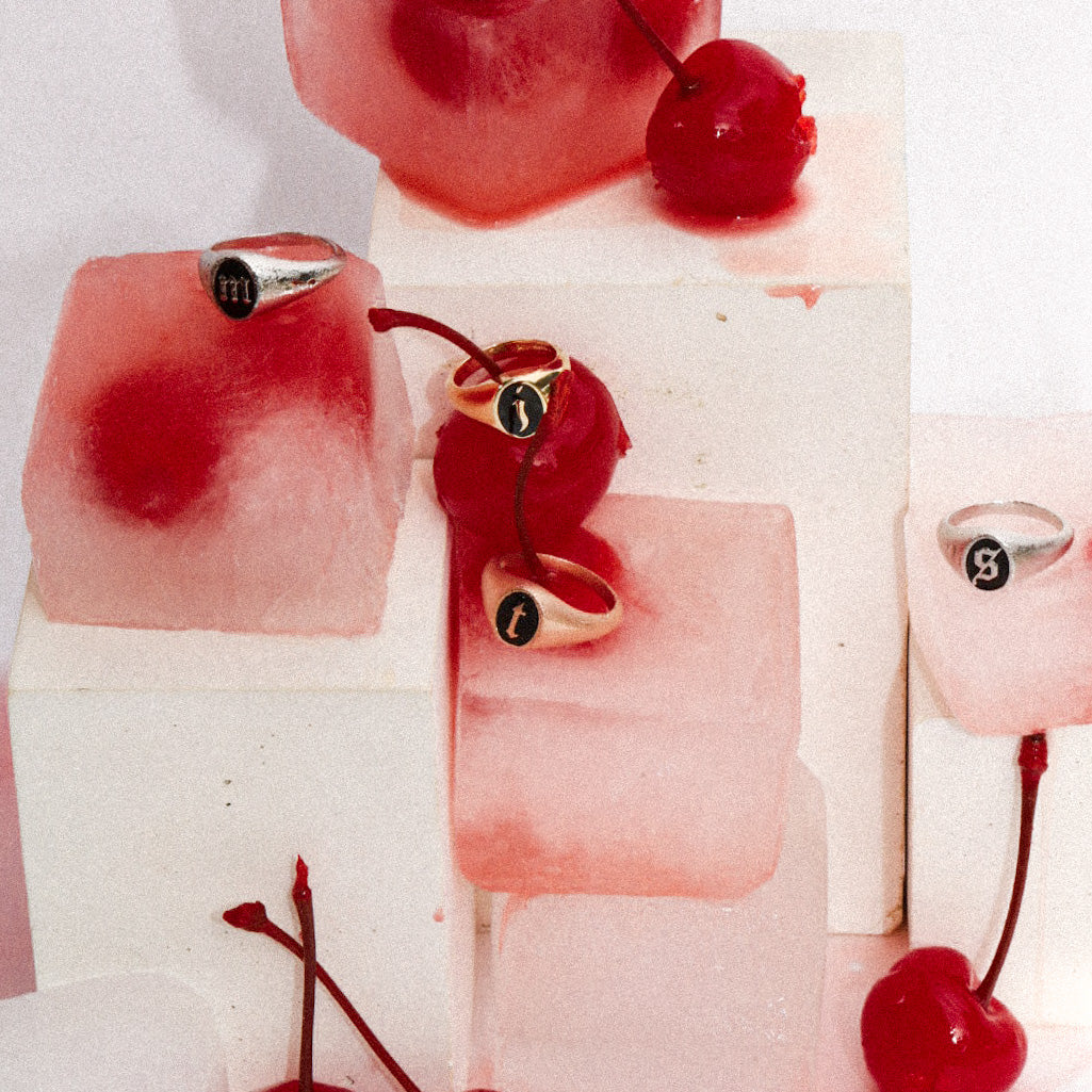 Lifestyle image of various Marrow Fine Initial Enamel Signets styled with ice cubes & cherries