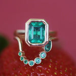 Ring with emerald and smaller gemstones on a red strawberry background
