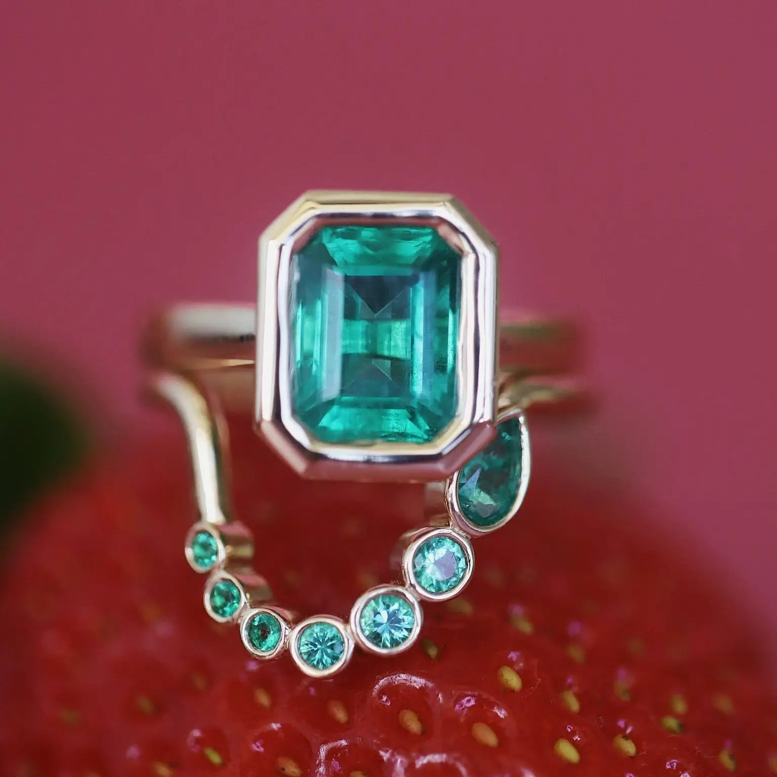 Ring with emerald and smaller gemstones on a red strawberry background