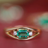 Gold ring with a green gemstone and smaller diamonds on a red background