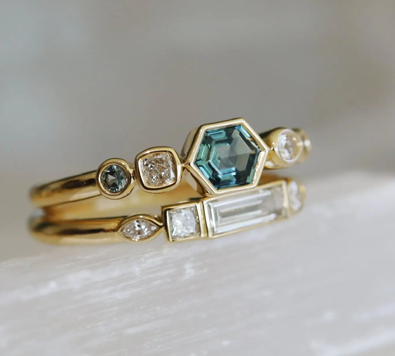 Two gold rings with gemstones on a light background