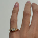 A close-up of a hand wearing a yellow gold signet ring with a pear-cut diamond in a bezel setting, against a plain light gray background.