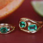 Two gold rings with emerald stones on a red surface.