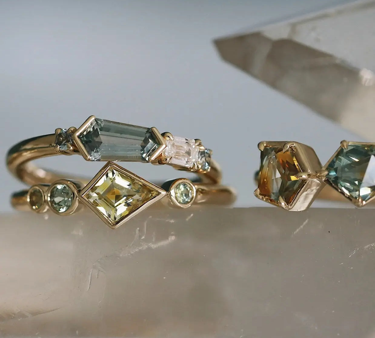 Three gold rings with gemstones on a reflective surface