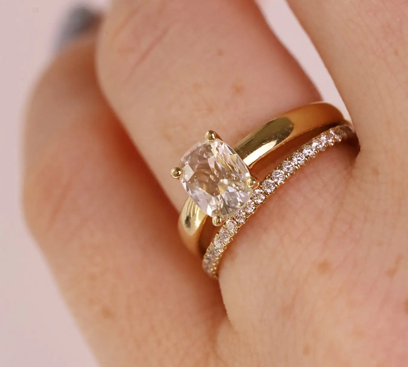 Close-up photo of a cushion cut diamond engagement ring stacked with a white diamond pave band
