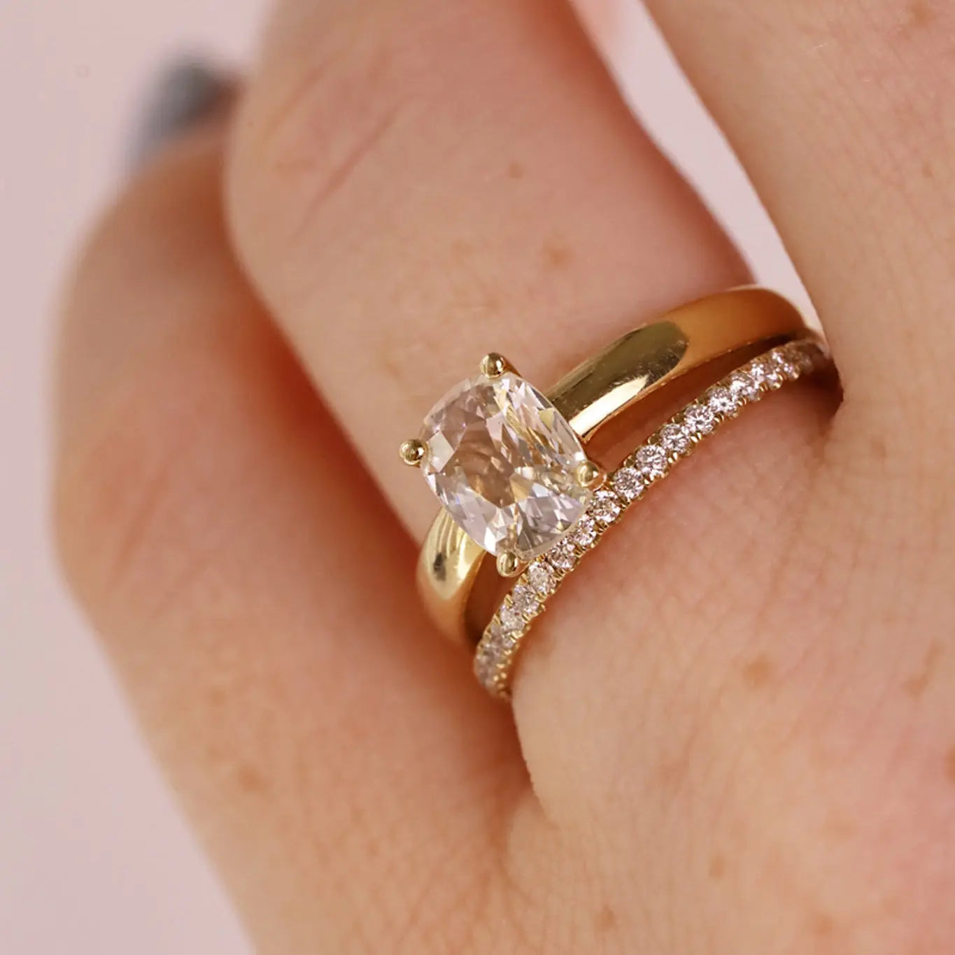 Close-up photo of a cushion cut diamond engagement ring stacked with a white diamond pave band