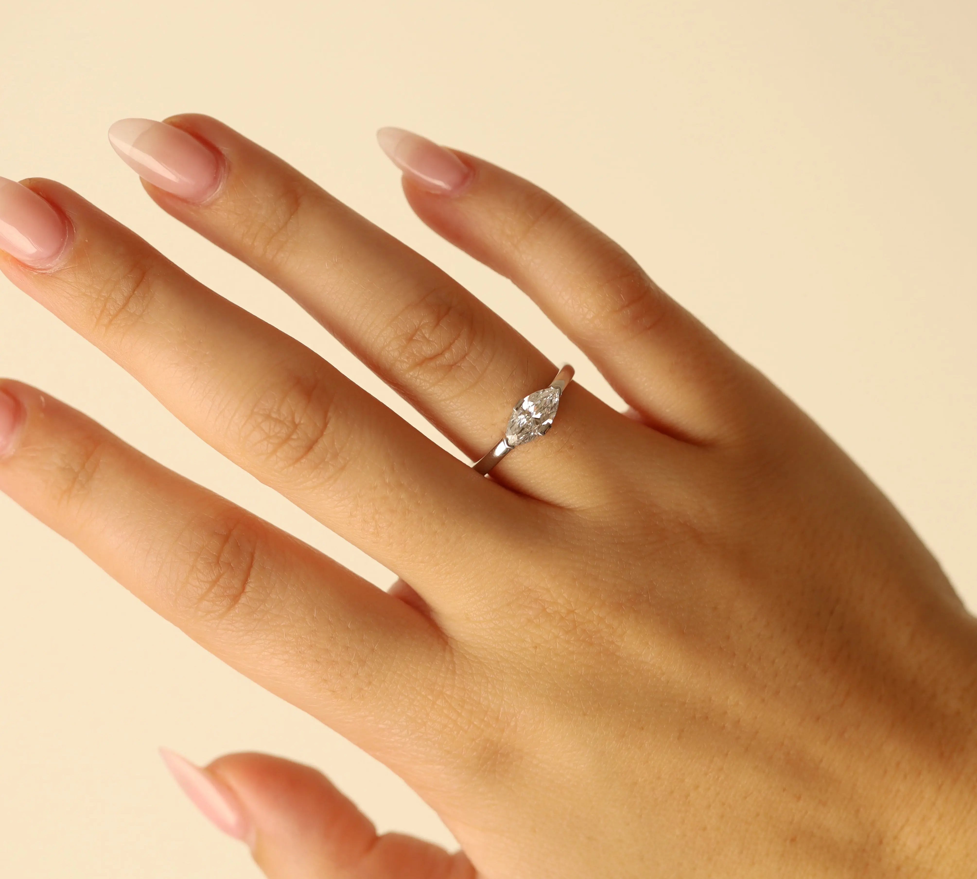 Hand wearing a white gold ring with a diamond on a beige background