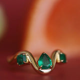 Gold ring with emerald green gemstones on a blurred background