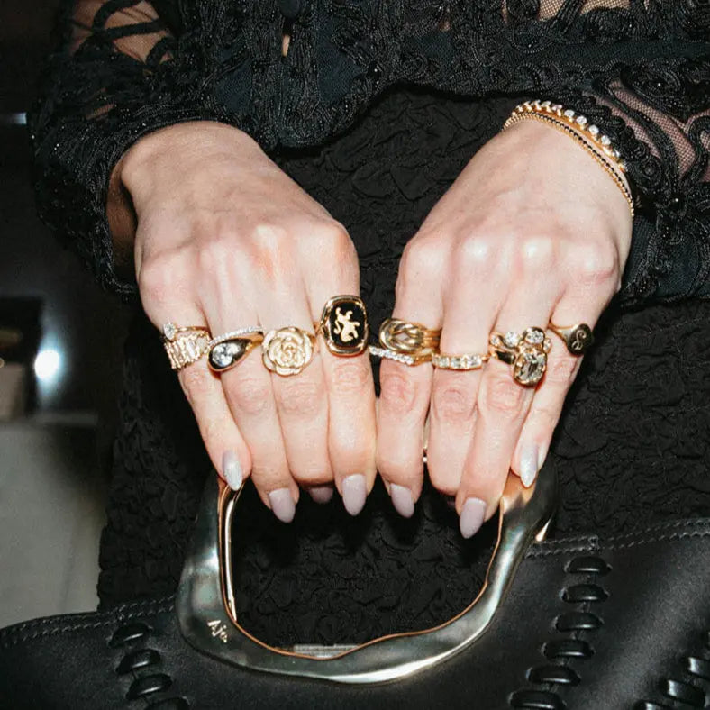 Person holding a black handbag with intricate detailing, wearing multiple rings on their fingers.