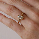 Gold ring with a diamond on a person's finger against a neutral background