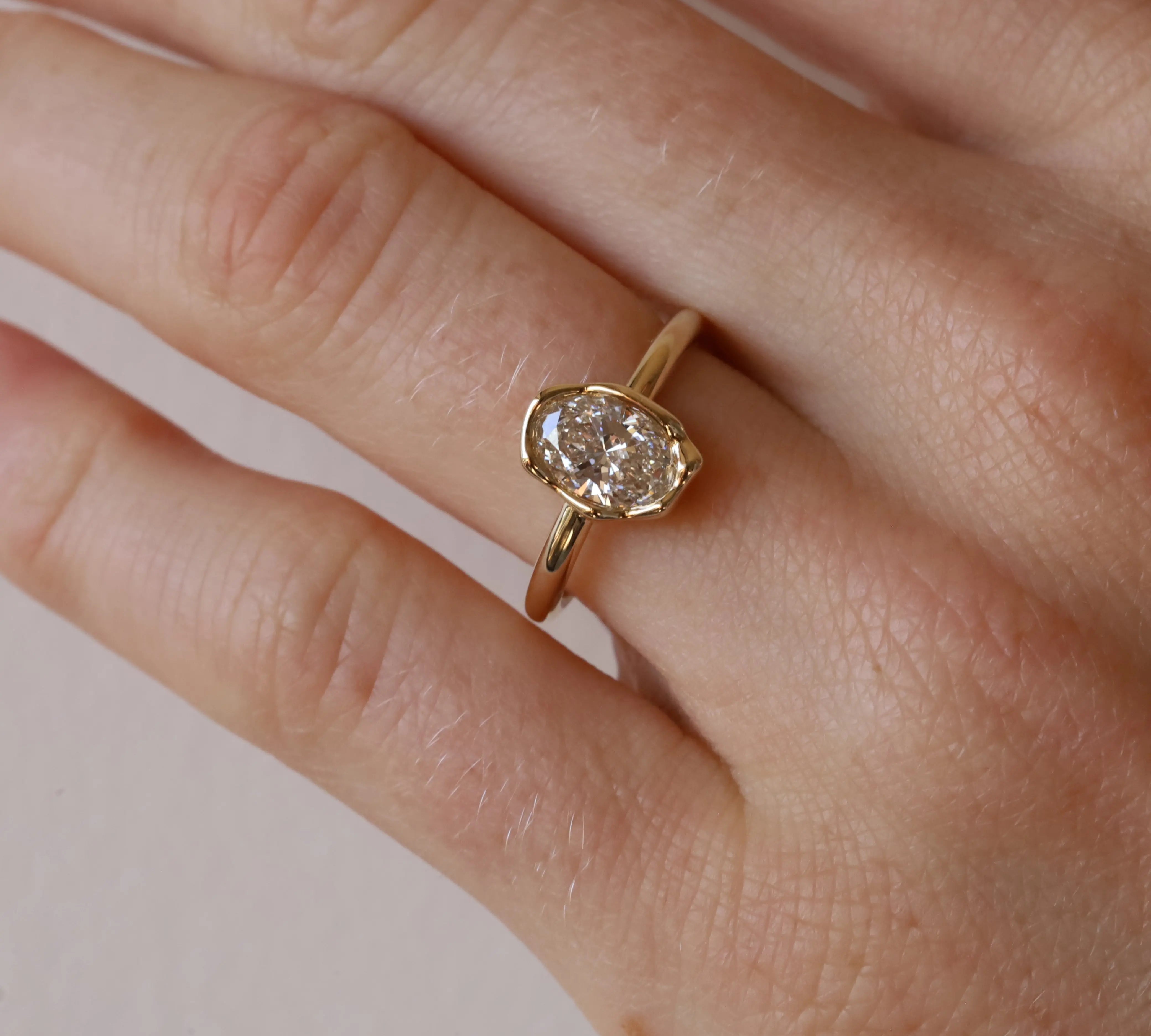 Gold ring with a diamond on a person's finger against a neutral background