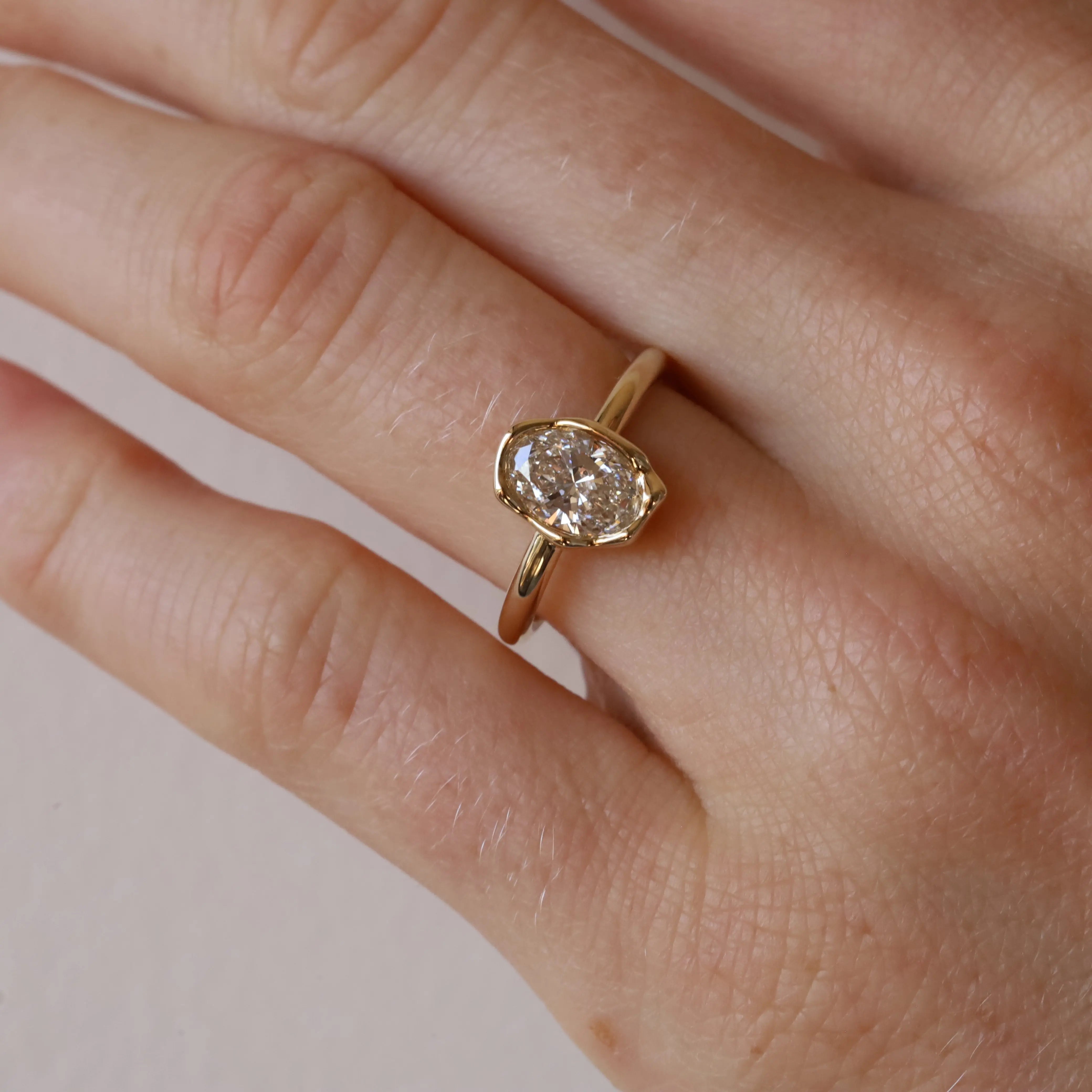 Gold ring with a diamond on a person's finger against a neutral background