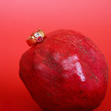 Red pomegranate with a gold ring featuring a red gemstone on a red background