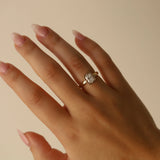 Hand wearing a gold ring with a diamond on a beige background