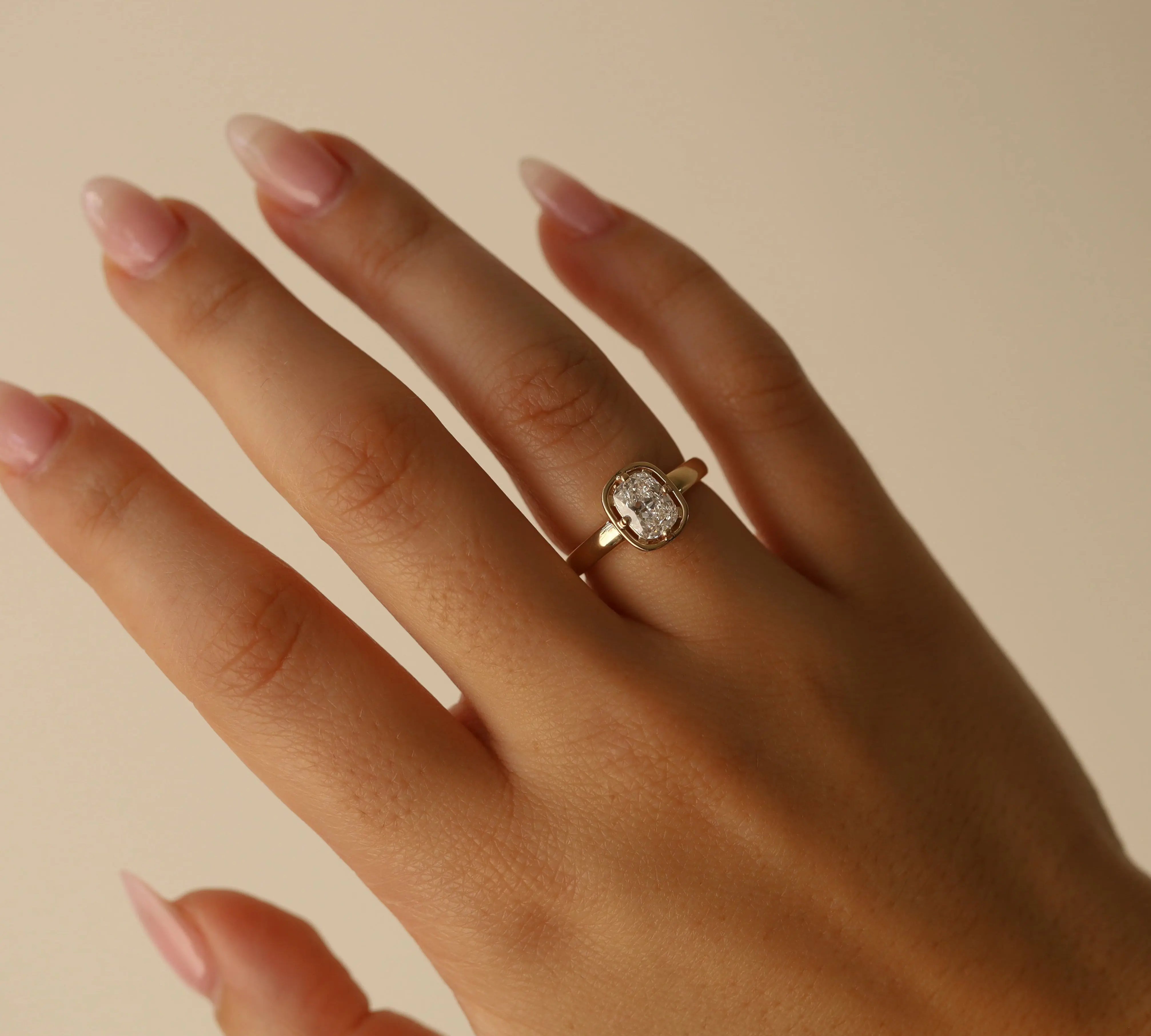 Hand wearing a gold ring with a diamond on a beige background