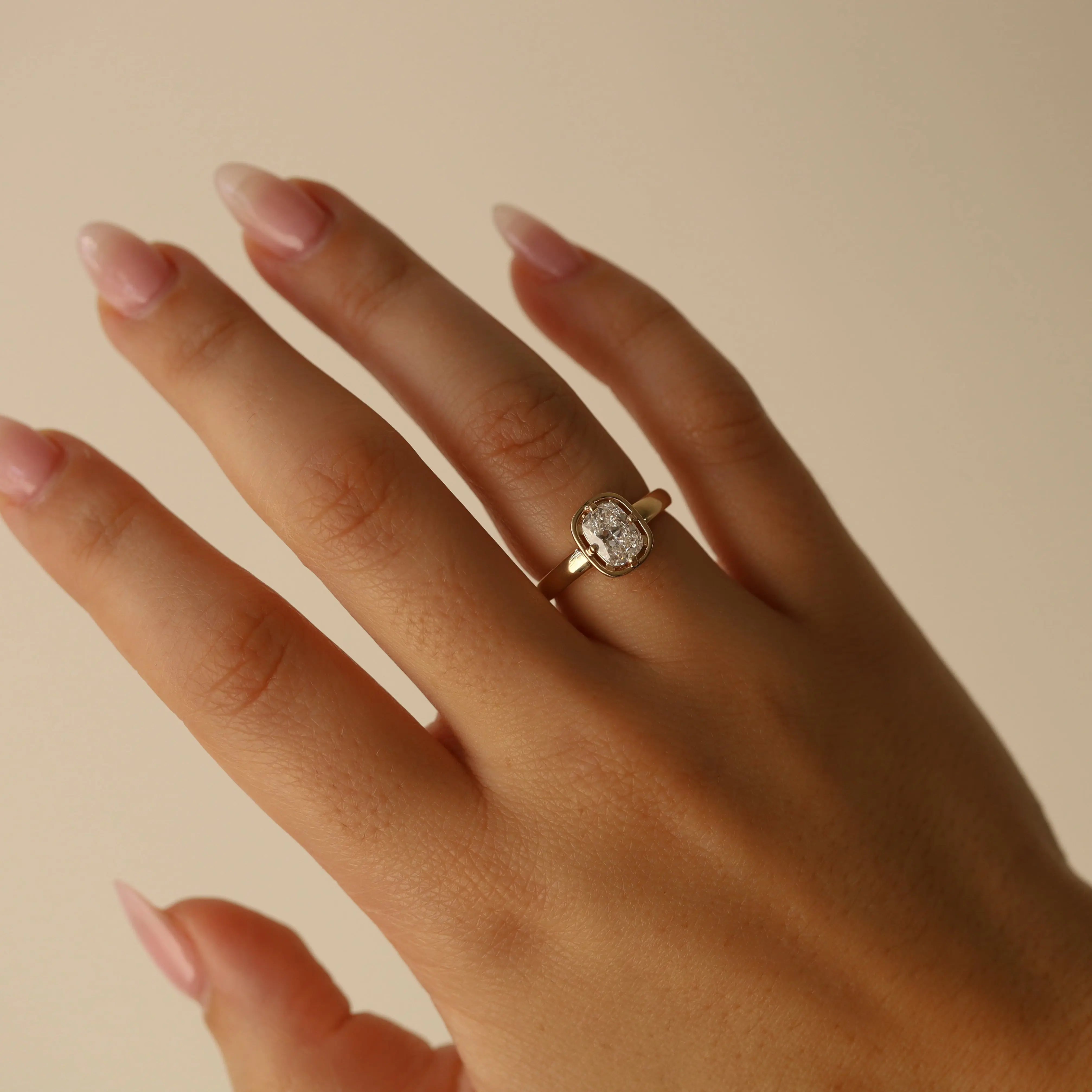 Hand wearing a gold ring with a diamond on a beige background