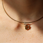 A close-up of a person's neck wearing a delicate gold collar necklace with a small abstract bezel gold pendant featuring a orange citrine stone and a small diamond rondelle.