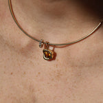 A close-up of a delicate gold necklace worn on a person's neck, featuring a small gold abstract bezel charm with a yellow citrine gemstone and a small diamond rondelle.