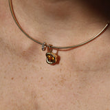 A close-up of a delicate gold necklace worn on a person's neck, featuring a small gold abstract bezel charm with a yellow citrine gemstone and a small diamond rondelle.