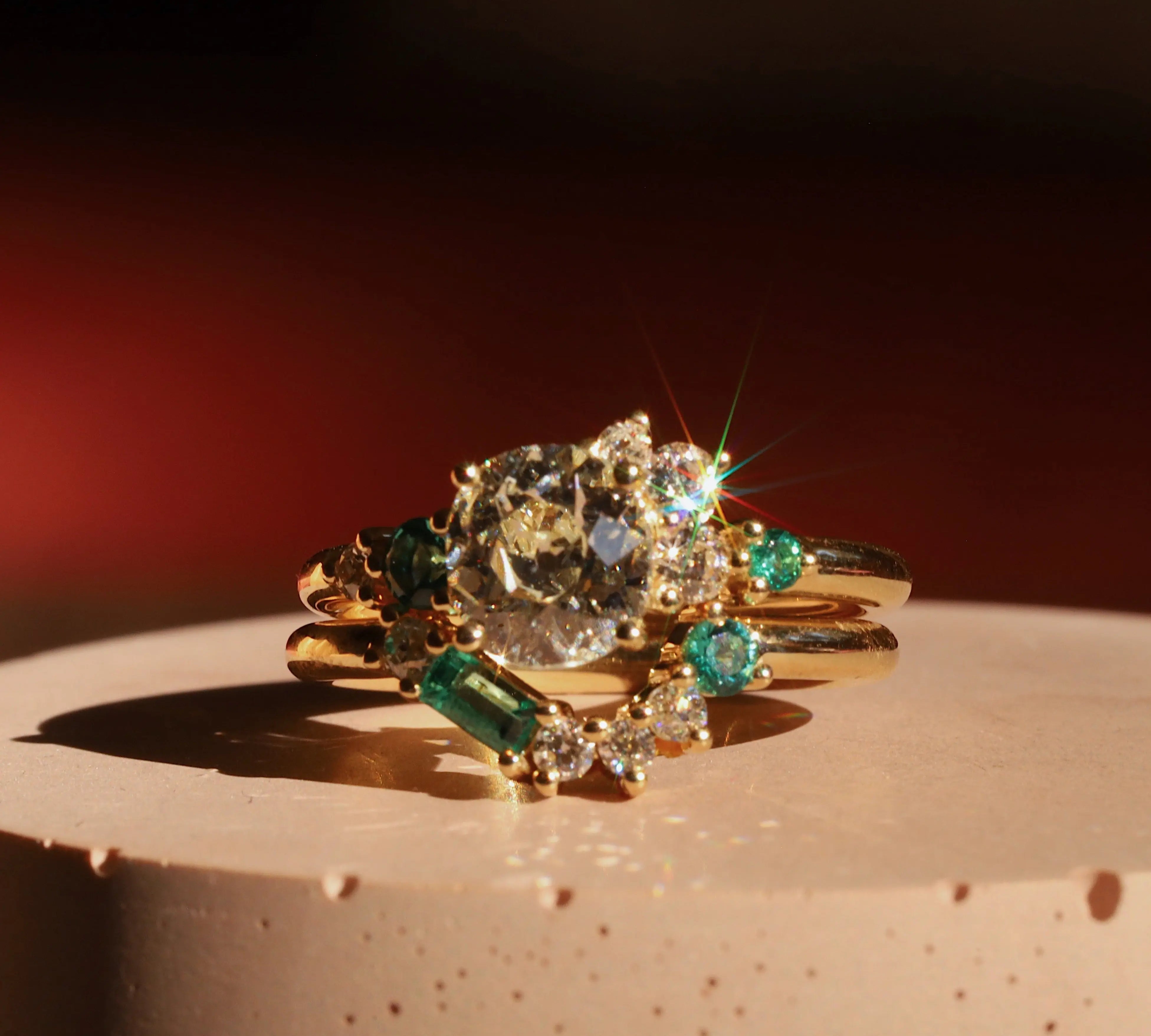 Gold ring with emerald and diamond stones on a textured surface