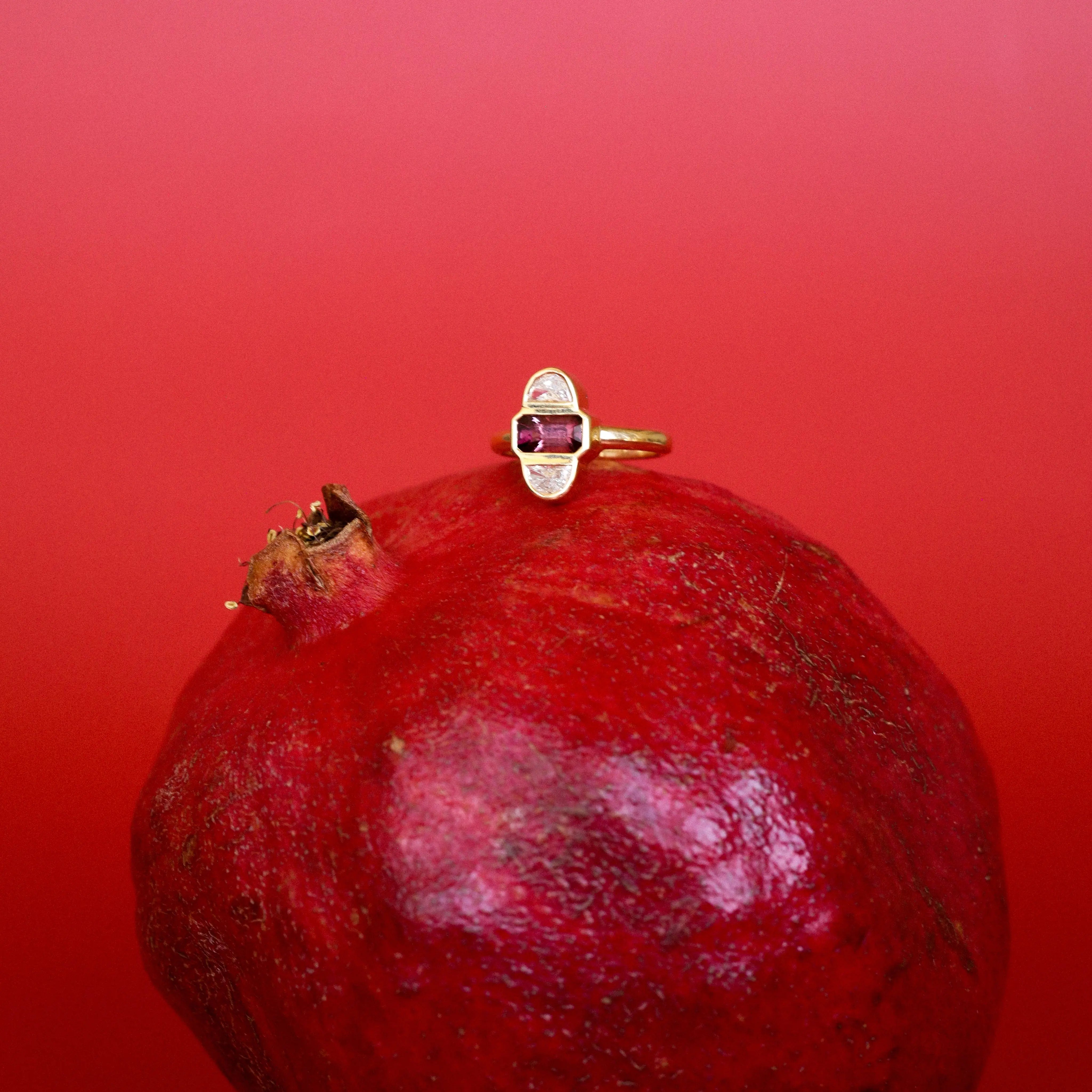 Gold ring with a gemstone on a pomegranate against a red background