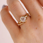 A close-up of a hand wearing a gold ring with a round clear gemstone in a prong setting, photographed against a soft light background.