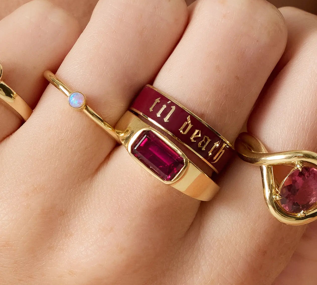 Gold ring with red gemstone and 'til death' engraving on a hand.