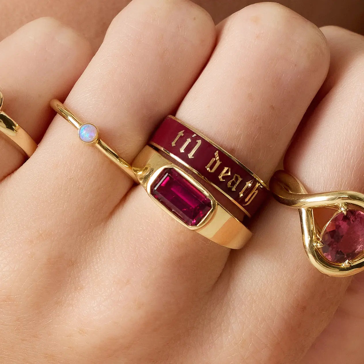 Gold ring with red gemstone and 'til death' engraving on a hand.