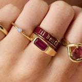 Gold ring with red gemstone and 'til death' engraving on a hand.