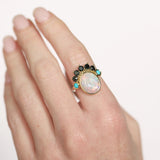 Ring with an opal stone and gemstones on a hand against a white background
