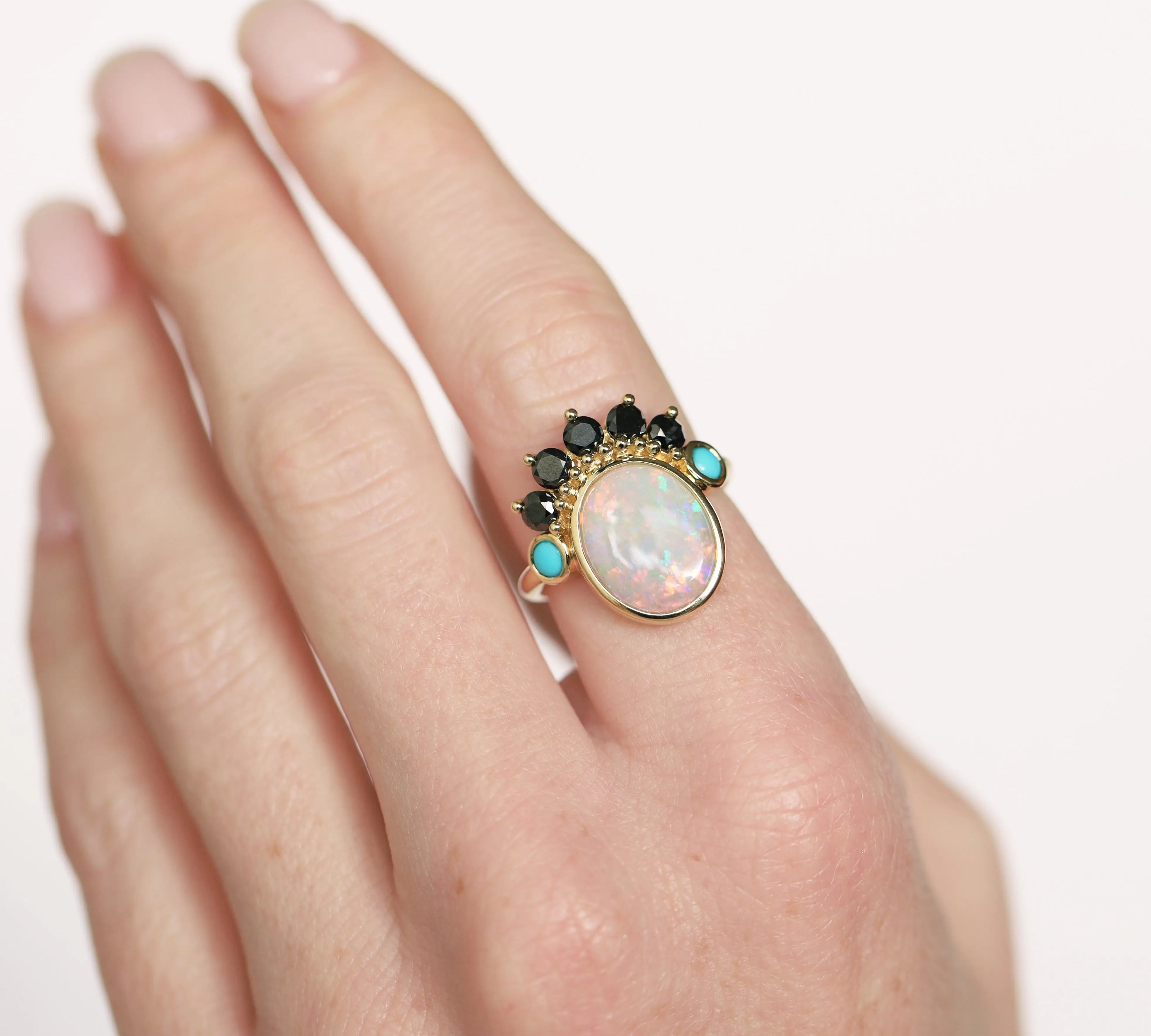 Ring with an opal stone and gemstones on a hand against a white background