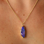 Gold necklace with a purple pendant on a person's neck